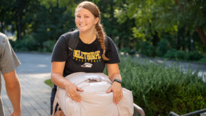A new student holds a bag of bedding, smiling while heading to her new dorm room.